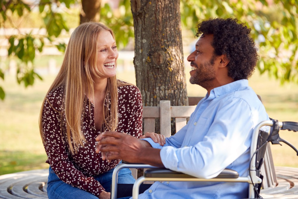 Mature Couple With Man Sitting In Wheelchair Talking In Park Together