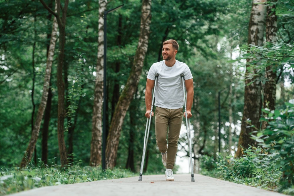 Man with crutches is in the park outdoors
